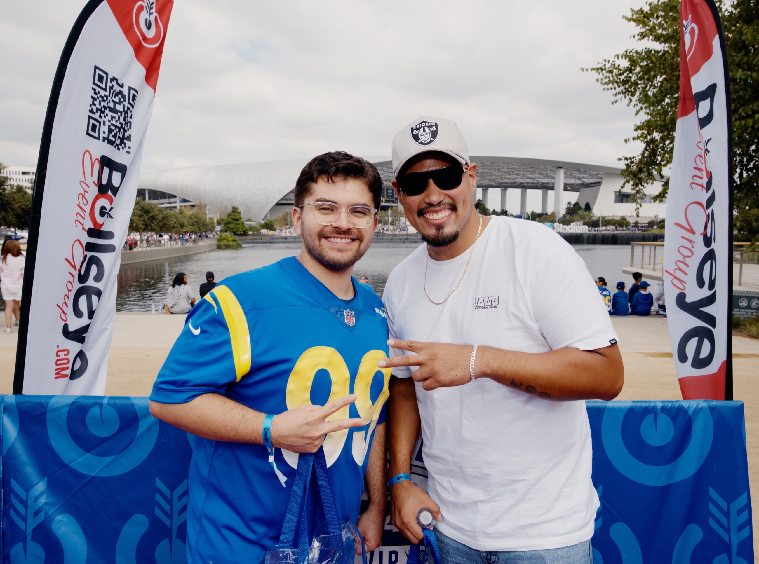 Two fans posing between branded event flags with the stadium in the background