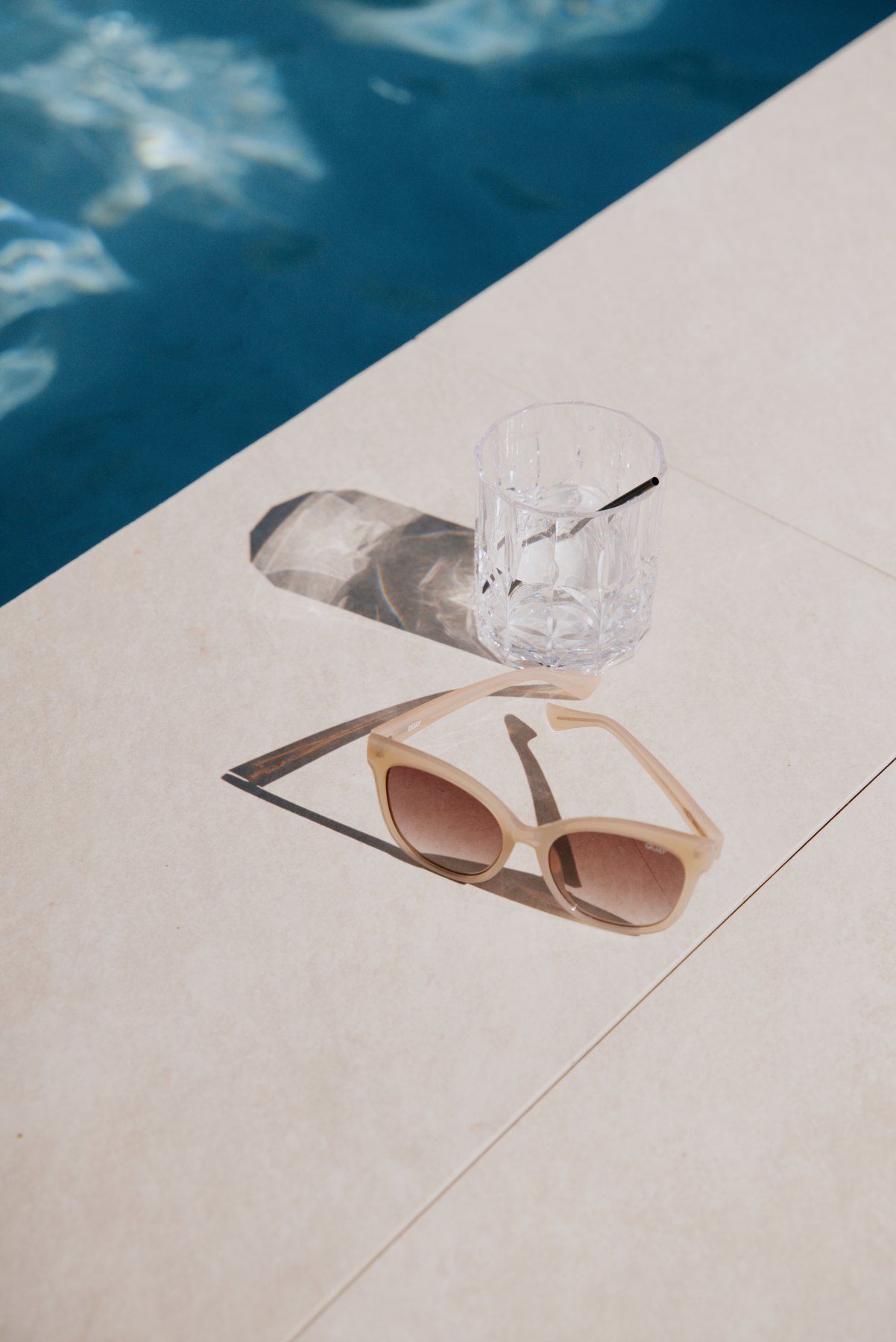 Sunglasses and glassware catching light beside a pool