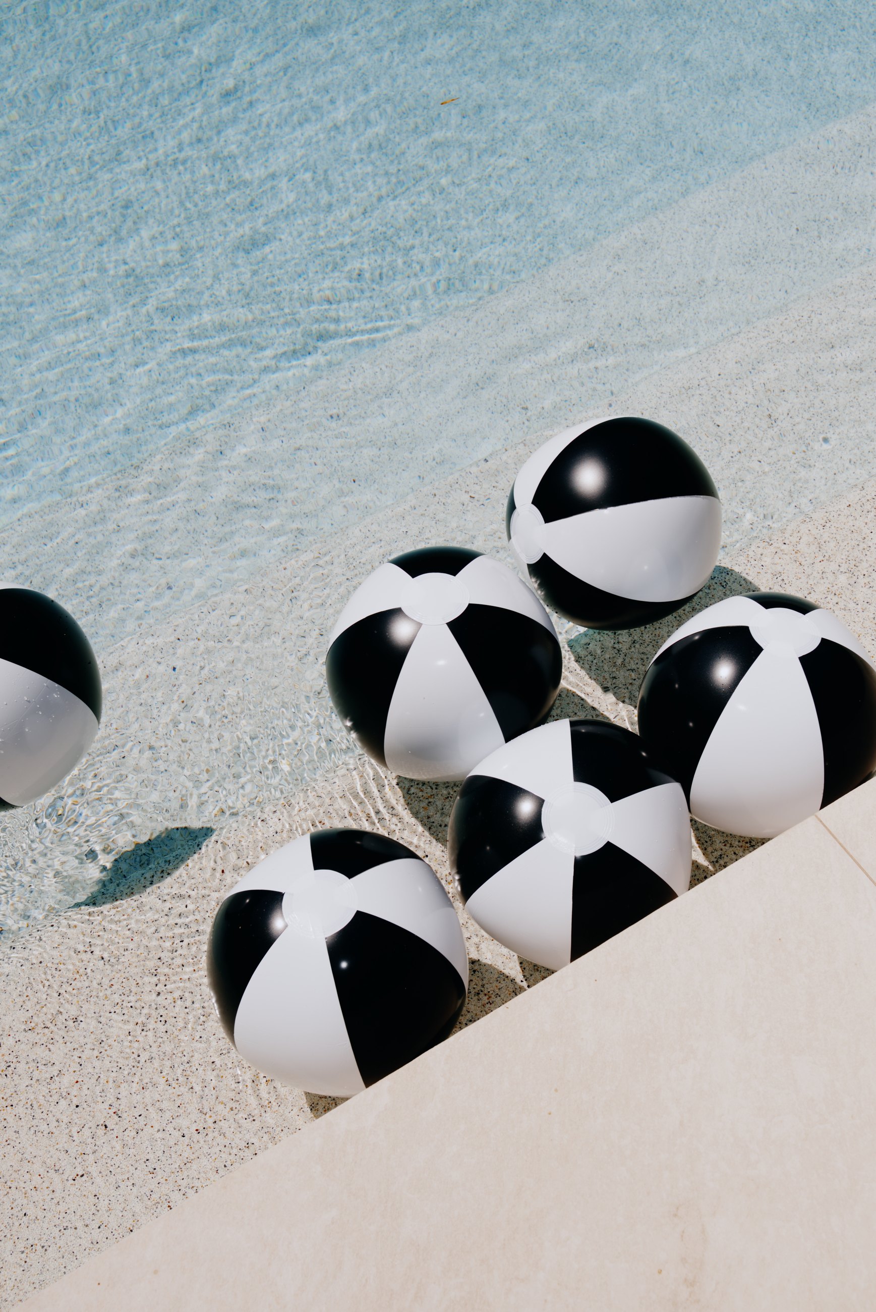 Black and white beach balls floating by a pool