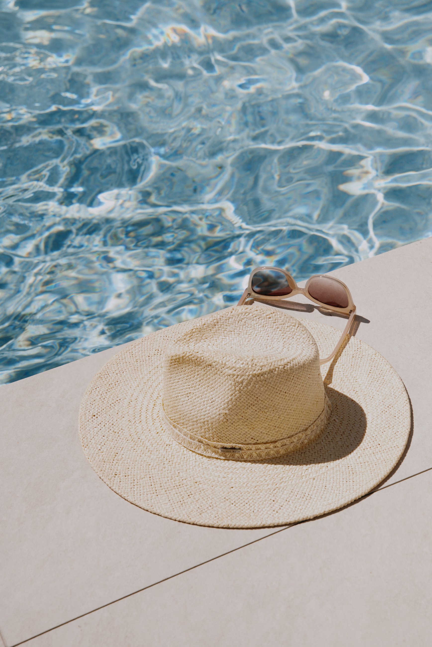 A sun hat and sunglasses beside bright pool water